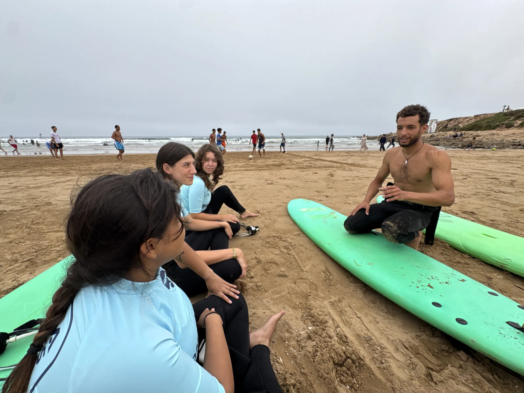 A surf coach talking with a small group beside their boards on the beach