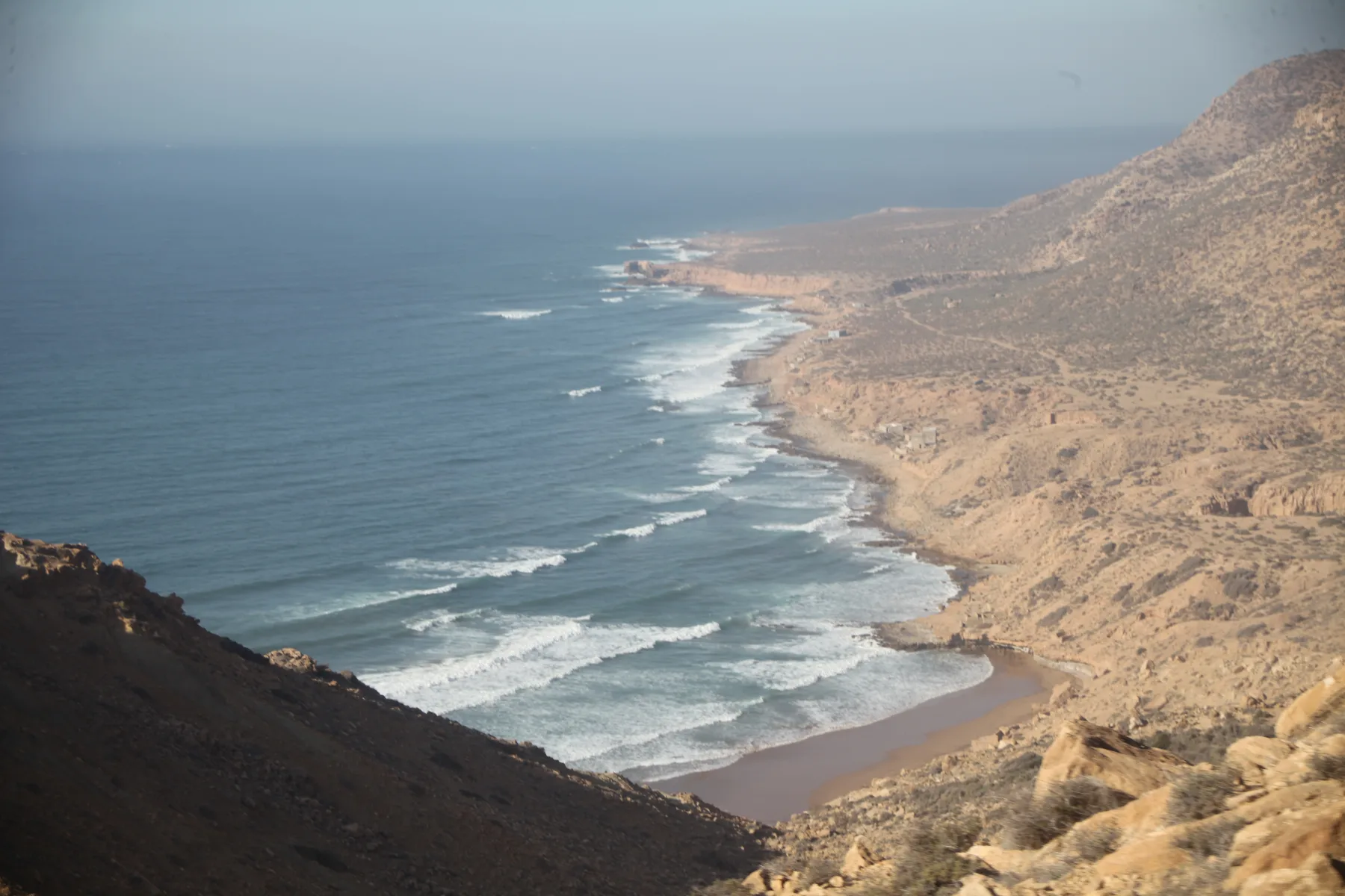 Atlantic waves meeting a long beach beneath coastal hills