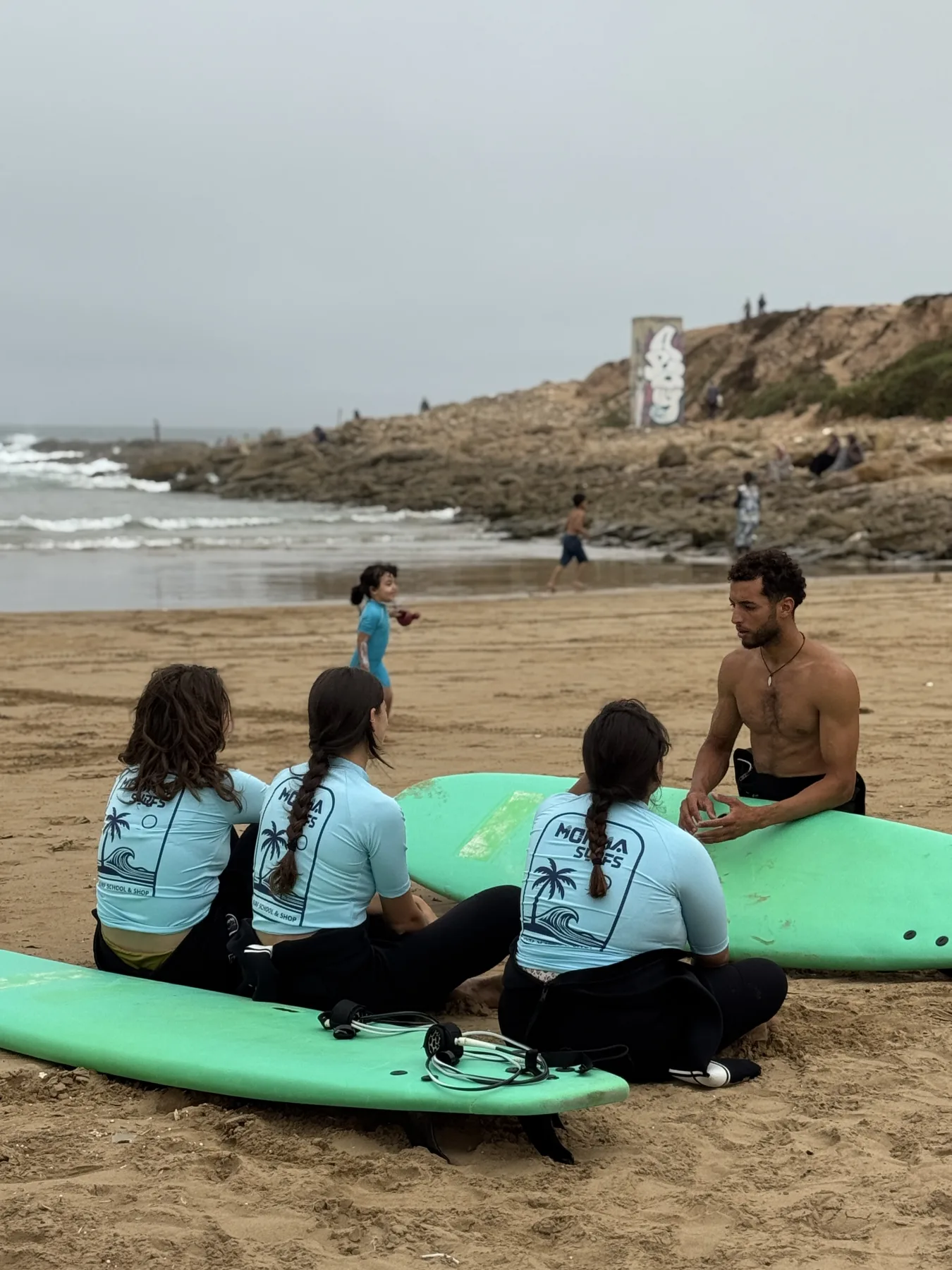 A Momma Surfs coach giving students a beach briefing beside their surfboards