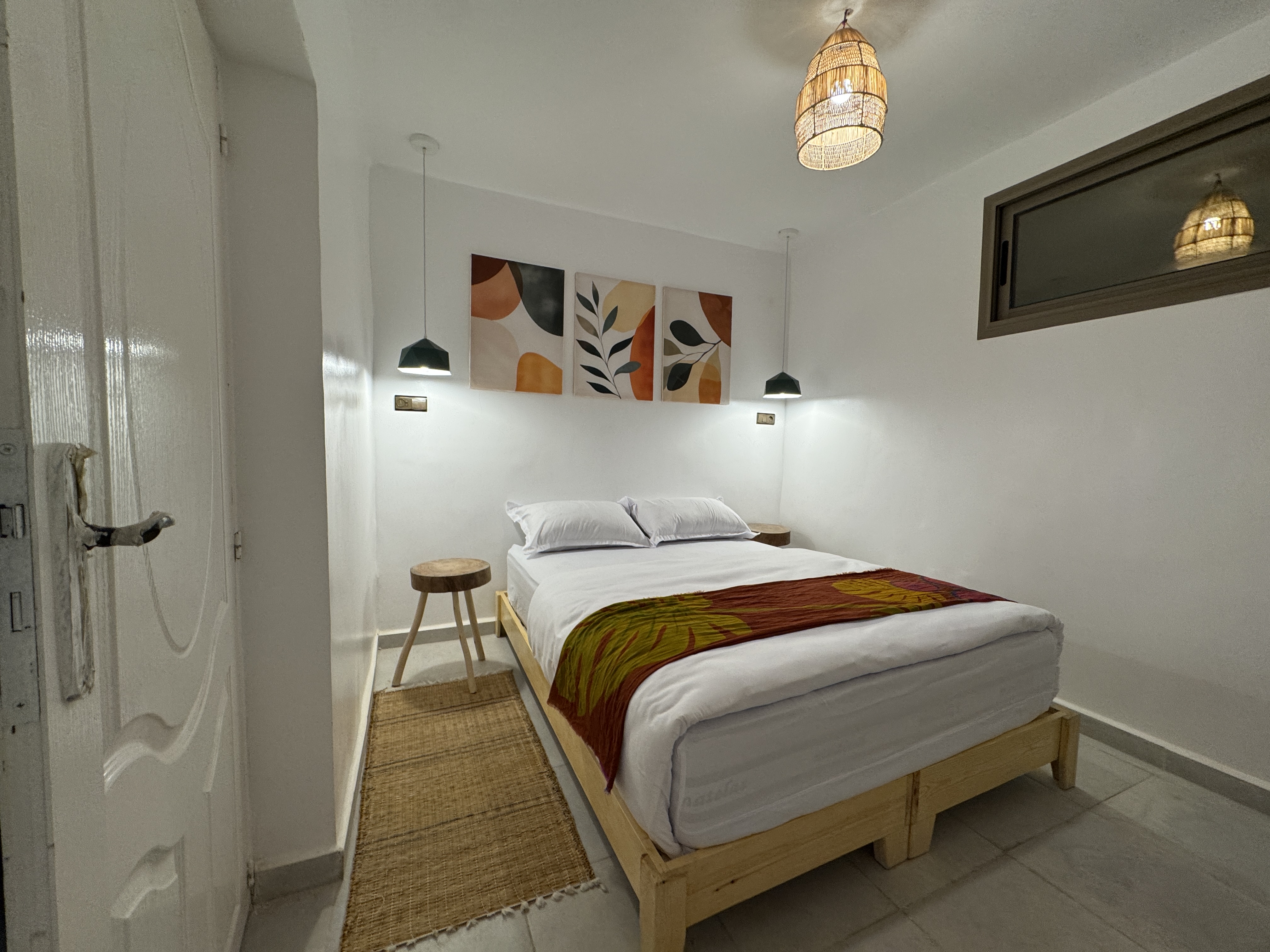 Finished double bedroom with white bedding, a warm patterned throw, wooden bedside tables and woven lighting