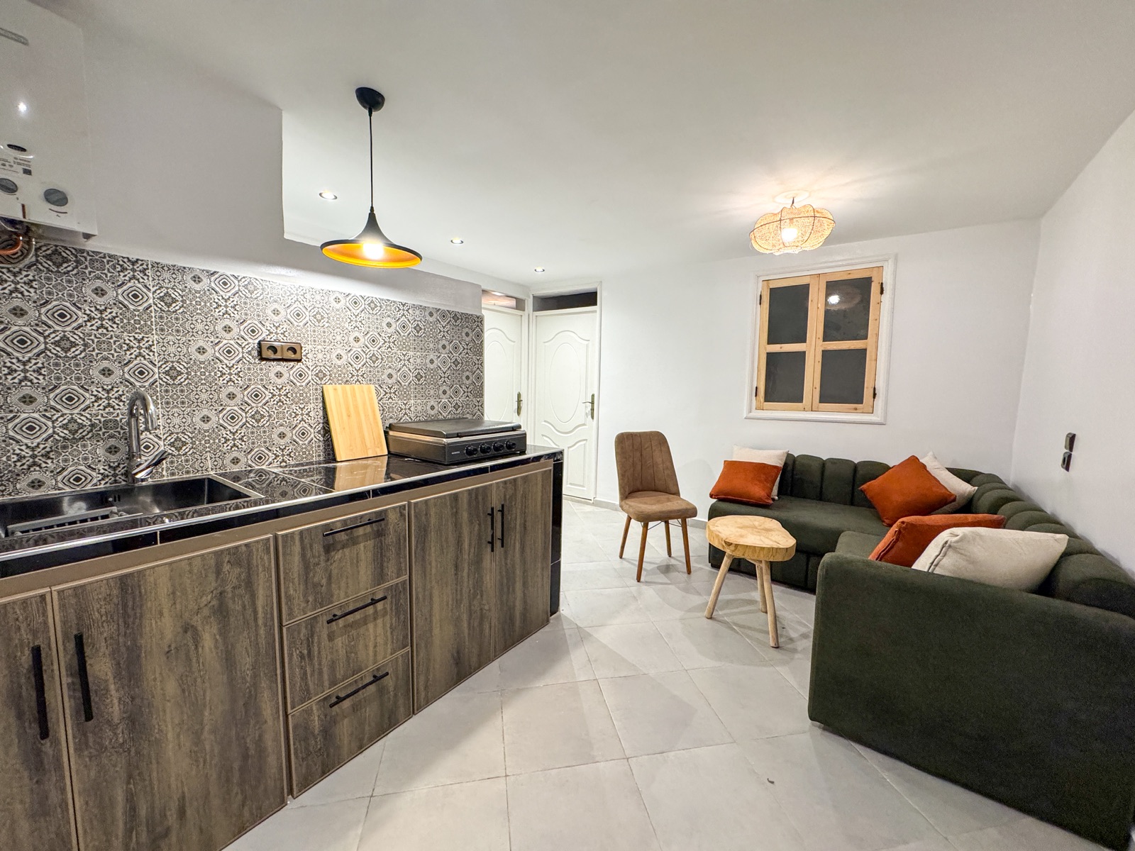 Shared kitchen with tiled backsplash beside a lounge with a green sofa and wooden coffee table