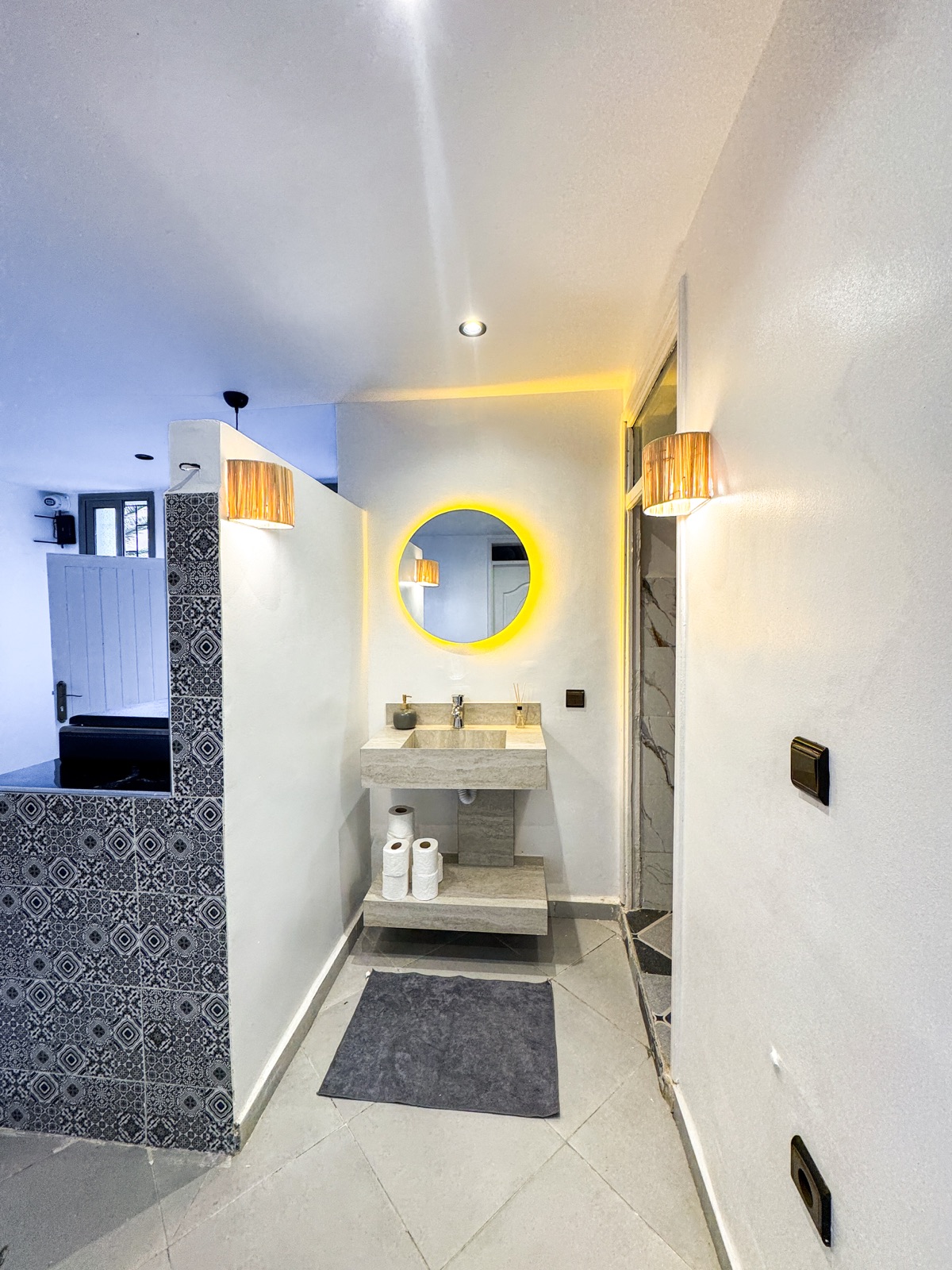 Shared wash area with a stone basin, illuminated round mirror and patterned tiles